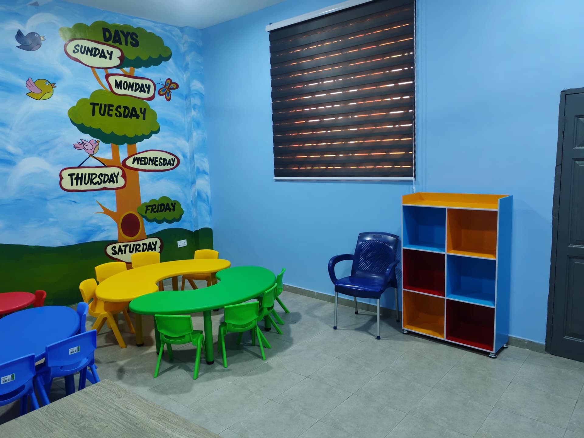 Kindergarten classroom corner with the days-of-the-week tree mural and a colourful storage shelf