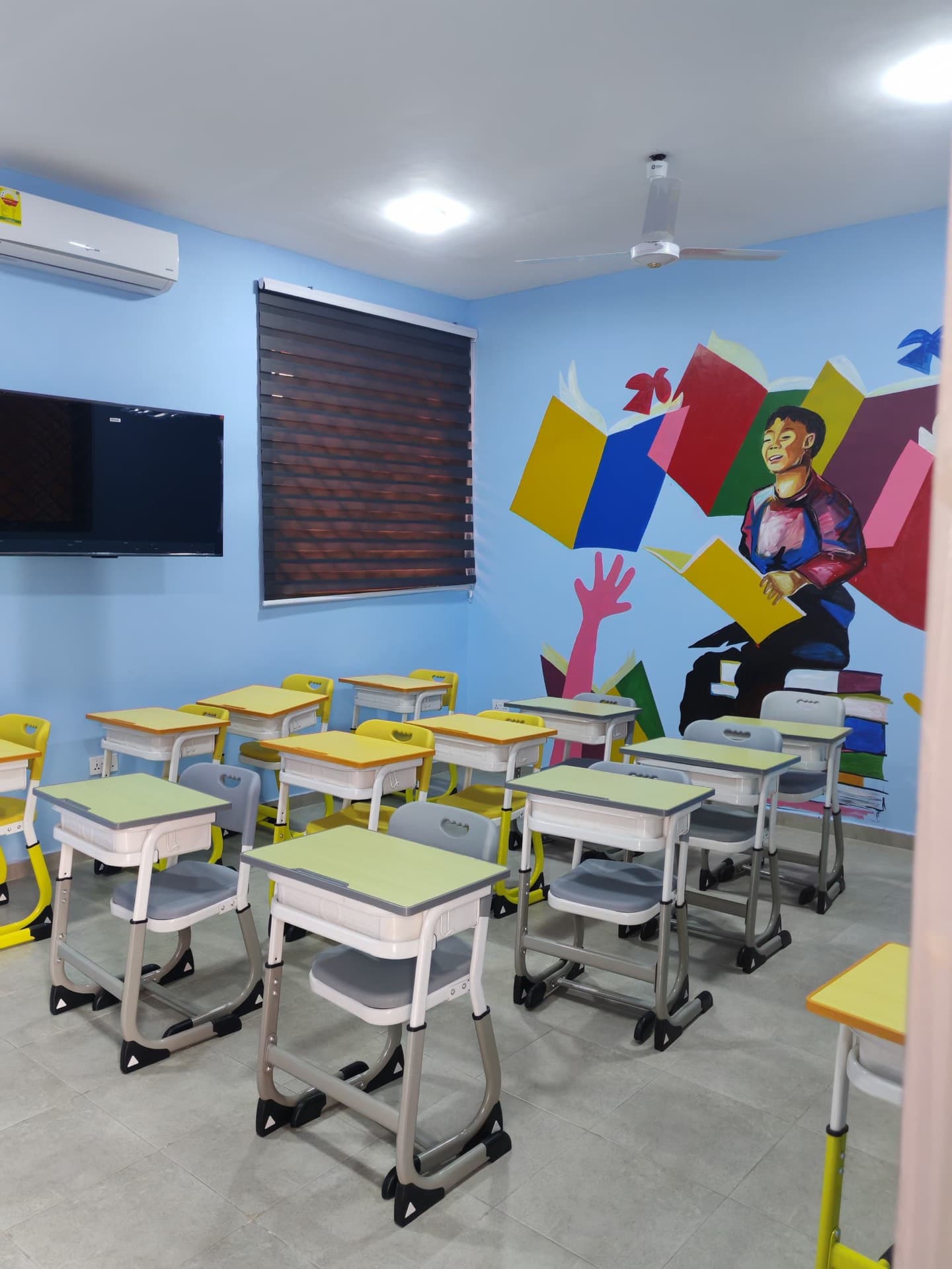 Primary classroom with rows of individual desks and a mural of a child reading a stack of books