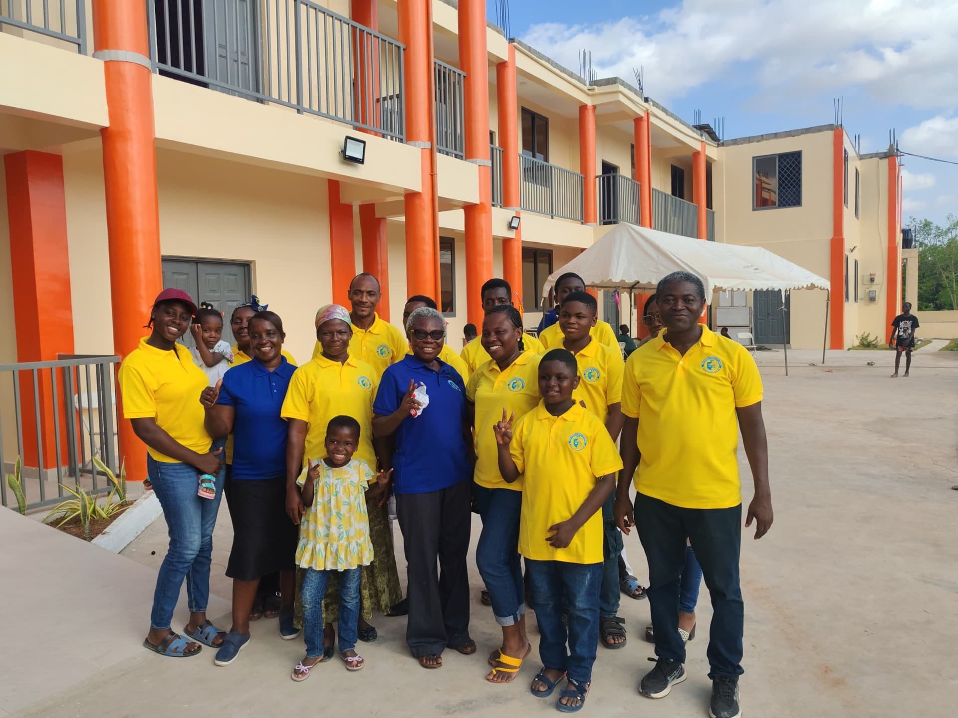 SLIS staff and community members in yellow and blue polo shirts posing in front of the school building