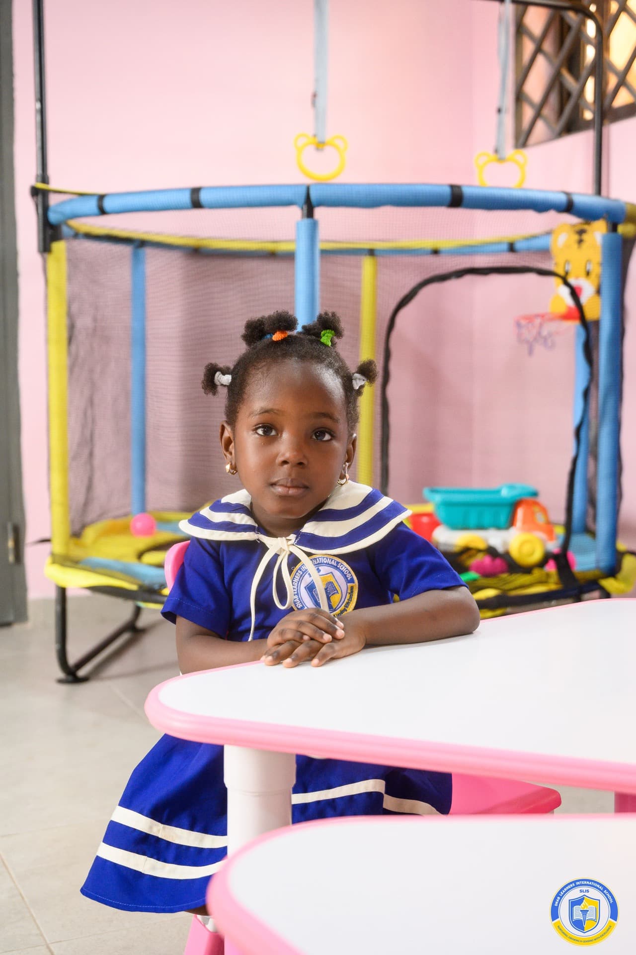 A young SLIS pupil in the school's blue sailor-collar uniform, seated at a play table